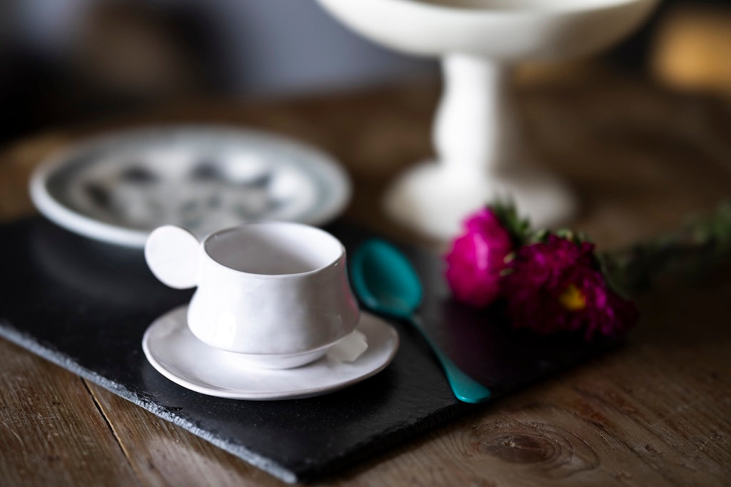 White ceramic cup and saucer on a dark surface with flowers and a blurred background
